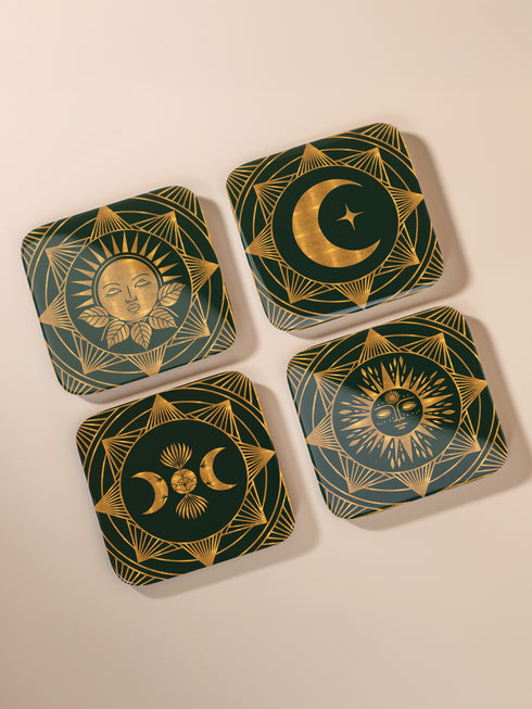 A set of four square coasters with a glossy finish, featuring celestial gold designs on a deep forest green background. Each coaster showcases a unique motif: a stylized sun with a serene face, a crescent moon with a star, a triple moon symbol with botanical elements, and a radiant sunburst. The intricate gold linework creates an art deco-inspired, mystical aesthetic. Made from durable materials, these coasters blend elegance with celestial charm.